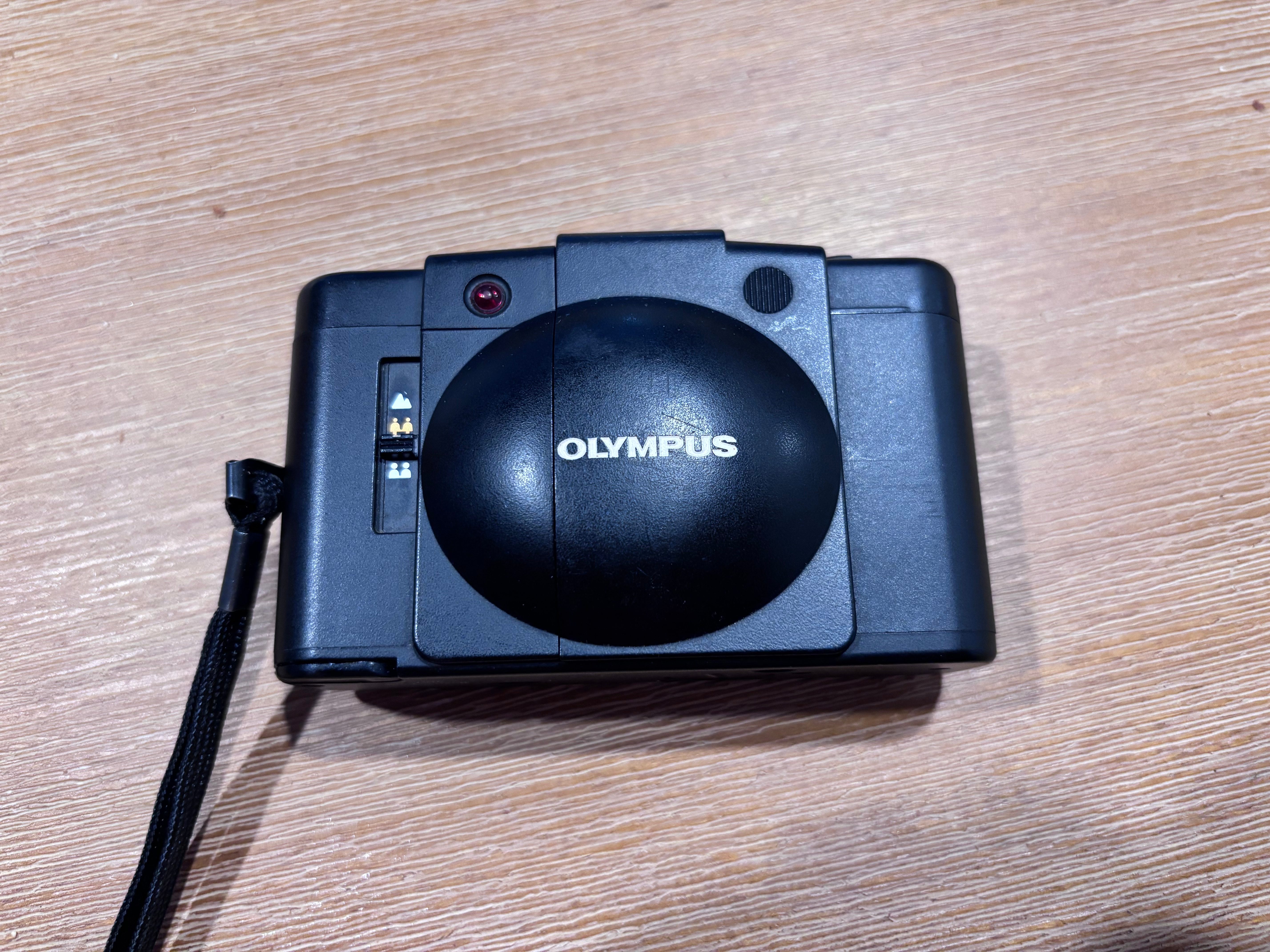 Top view of an Olympus camera resting on a wooden surface.